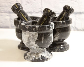 May include: Three black and white marble mortars and pestles of varying sizes. The mortars are round and have a wide base. The pestles are cylindrical and fit snugly inside the mortars.