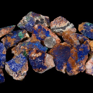 May include: A pile of rough, raw azurite and malachite stones. The stones are a mix of blue, green, brown, and white. A US quarter is included for scale.