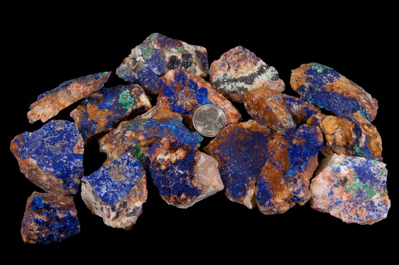 May include: A pile of rough, raw azurite and malachite stones. The stones are a mix of blue, green, brown, and white. A US quarter is included for scale.