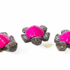 May include: Three small pink and black turtle figurines. The turtles are made of wood and have a glossy finish.