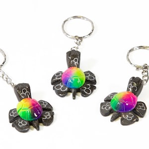 May include: Three black wooden turtle keychains with rainbow colored shells. Each keychain has a silver ring and chain.