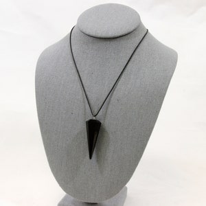 Può includere: Ciondolo a punta di ossidiana nera su una collana con cordoncino nero. Il ciondolo ha una forma appuntita ed è appeso a un semplice cordoncino nero.