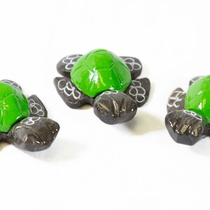 May include: Three small green and black turtle figurines. The turtles have a glossy green shell and a black body with white floral designs.