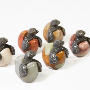 May include: Six small, hand-carved stone turtle figurines. Each turtle is depicted emerging from a round, multi-colored egg. The eggs are made of different types of stone, including white, brown, orange, and red.