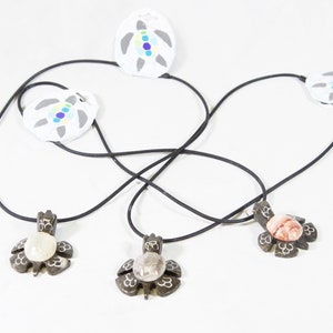 May include: Three necklaces with turtle-shaped pendants. Each pendant is made of wood and has a different colored stone in the center. The necklaces are on a white background.