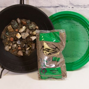 May include: A black metal pan containing a variety of rocks and minerals, a green plastic sifting pan, and a bag of sand labelled "Emerald Bag".