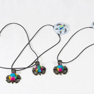 May include: Three necklaces with turtle-shaped pendants. Each pendant features a colorful, mosaic-like design in shades of blue, green, yellow, and pink. The pendants are connected to a black cord.