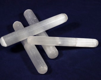 Puede incluir: Un conjunto de cuatro varitas de selenita cilíndricas con una apariencia fibrosa, blanca y translúcida. Cada varita presenta una forma alargada y lisa con extremos redondeados, mostrando la textura natural, reflectante y estratificada.