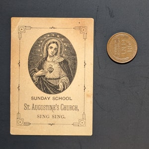 May include: A vintage Sunday School card featuring a black and white illustration of the Virgin Mary with a heart in her chest. The card has a decorative border and the text "SUNDAY SCHOOL ST. AUGUSTINE'S CHURCH, SING SING."