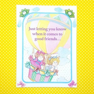 May include: A greeting card with a colorful hot air balloon illustration. Two dolls are riding in the balloon. The text on the card reads "Just letting you know when it comes to good friends..."