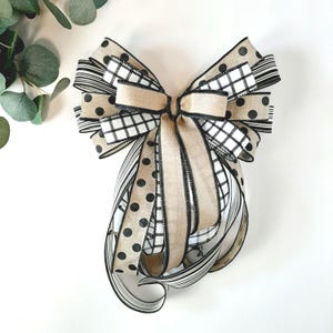 May include: A decorative bow featuring a mix of patterns, including polka dots, stripes, and a checkered design. The bow incorporates beige, black, and white ribbons, creating a layered effect. The bow is likely used for gift wrapping or home decor.