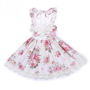 May include: A white sleeveless dress with a floral print and lace trim. The dress has a tie at the back and a ruffled neckline.