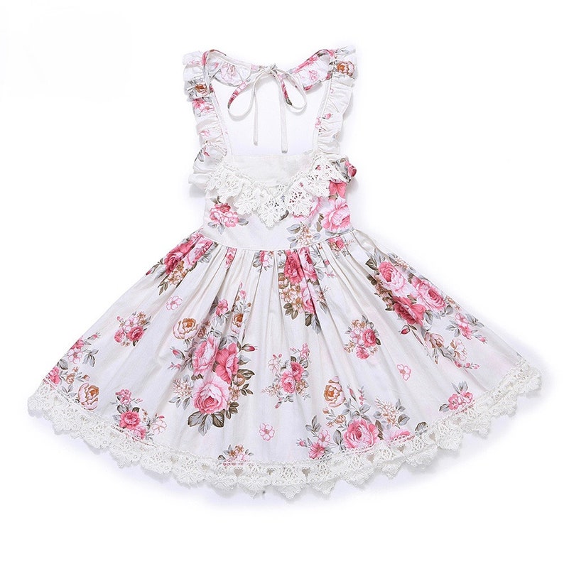May include: A white sleeveless dress with a floral print and lace trim. The dress has a tie at the back and a ruffled neckline.