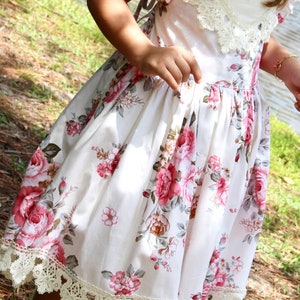 May include: A white dress with a floral print and lace trim. The dress has a scoop neck and a fitted bodice. The skirt is full and flowing.