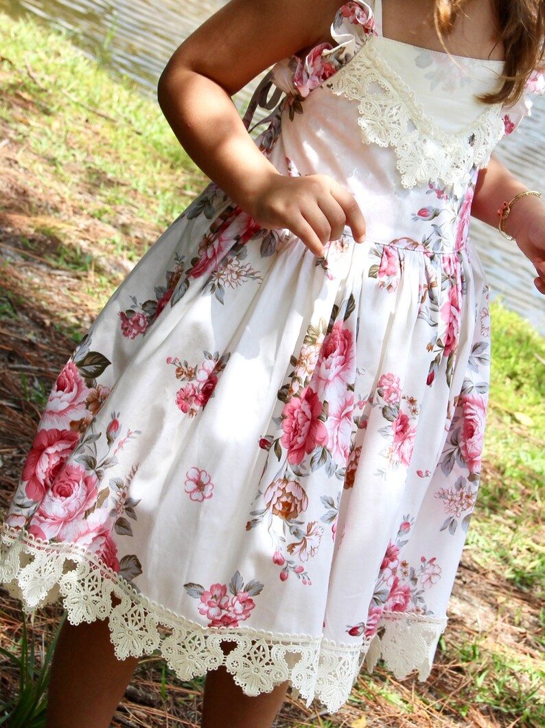 May include: A white dress with a floral print and lace trim. The dress has a scoop neck and a fitted bodice. The skirt is full and flowing.