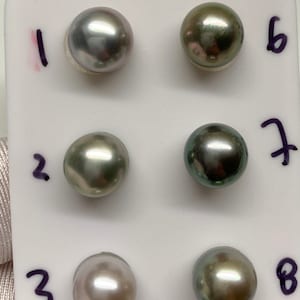 May include: Eight round pearls, numbered 1 through 8, displayed on a white surface. The pearls are a mix of gray and green colors.
