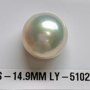 May include: A large, lustrous pearl with iridescent green and pink hues. The pearl is approximately 0.59 inches in diameter. A white label below the pearl displays the text "SS - 14.9MM LY - 510275".