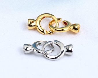 May include: Two metal jewellery clasps. One is gold-coloured, and the other is silver-coloured. Each clasp has a circular design with a connecting mechanism. The clasps are on a white background.