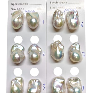 May include: Close-up of two white cards displaying irregularly shaped pearls. Each card has a series of pearls, numbered 1 through 8. The pearls have a lustrous, iridescent sheen, reflecting colors like pink, green, and gold.