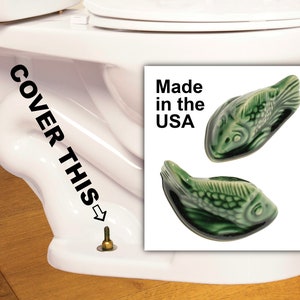 May include: Two green ceramic fish-shaped toilet bolt covers. The covers are displayed on a white background. The text "Made in the USA" is visible. The covers are designed to conceal the toilet bolts.
