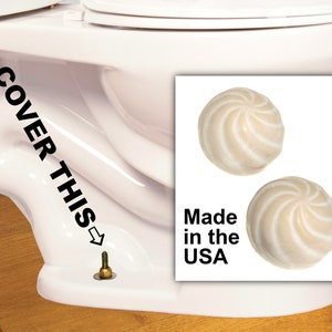 May include: Close-up of a white toilet bowl with a screw visible underneath. The text "COVER THIS" is written on the side of the toilet bowl with an arrow pointing to the screw. Two white toilet bowl cleaner balls are shown in the image with the text "Made in the USA".