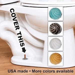 May include: White toilet with a swirl-design toilet bolt cap in four colors: teal, black and gray, white, and yellow. Text on the toilet reads "COVER THIS" and "USA made • More colors available."