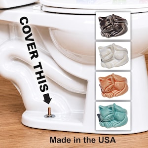 May include: White ceramic toilet with a decorative cat-shaped toilet bolt cover. The image shows four different colors of the cat-shaped cover: dark brown, white, orange, and teal. Text on the image reads "COVER THIS" and "Made in the USA."