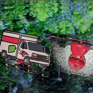 May include: A white delivery truck with red and green accents, a black front bumper, and a black back bumper. The truck is a pin with a red metal backing.
