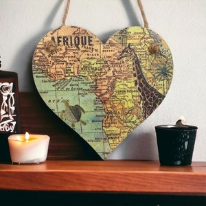 May include: A wooden heart-shaped ornament with a vintage map of Africa printed on it. The map shows the countries of Africa, including Nigeria, Cameroon, Congo Belge, and Angola. A giraffe and a turtle are also depicted on the map.