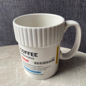 May include: White ceramic coffee mug with a prescription label design. The mug features the word "COFFEE" in bold letters, along with other text and a barcode. It has a capacity of 350ml.
