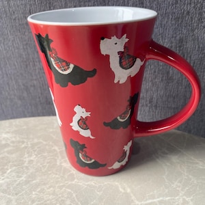 May include: Red ceramic mug with a white interior and a red handle. The mug is decorated with repeating illustrations of black and white Scottish Terrier dogs wearing tartan harnesses.