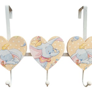 Puede incluir: Tres ganchos de metal blanco en forma de corazón con fondo amarillo y una imagen de dibujos animados de Dumbo el elefante. Cada gancho tiene un patrón de lunares blancos.