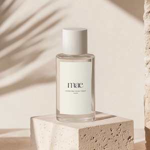 Könnte beinhalten: Eine durchsichtige Glasflasche mit weißem Verschluss und Etikett. Das Etikett trägt die Aufschrift "mae HYDRATING FACIAL TONER 100ml". Die Flasche steht auf einer hellbraunen, strukturierten Oberfläche.