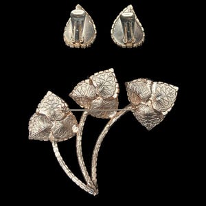 Vertical back view of 1960s vintage iridescent rhinestone and gold tone floral brooch and clip on earring jewelry set.