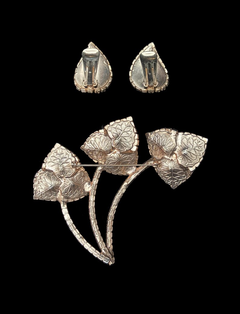 Vertical back view of 1960s vintage iridescent rhinestone and gold tone floral brooch and clip on earring jewelry set.