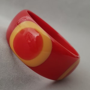 May include: Red and yellow plastic bangle bracelet with a geometric pattern.