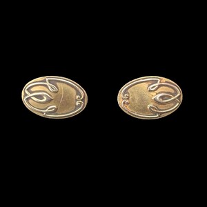 May include: A pair of gold oval cufflinks with a decorative design. The design features a stylized floral motif.