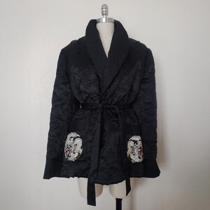 May include: A black quilted robe with a satin finish and a shawl collar. The robe has two pockets with embroidered white dragons on each side. The robe is tied with a black satin sash.