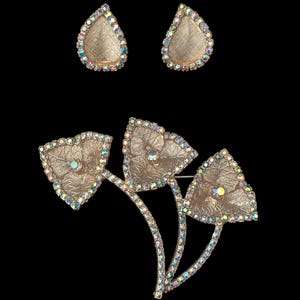 Vertical front view of 1960s vintage iridescent rhinestone and gold tone floral brooch and clip on earring jewelry set.