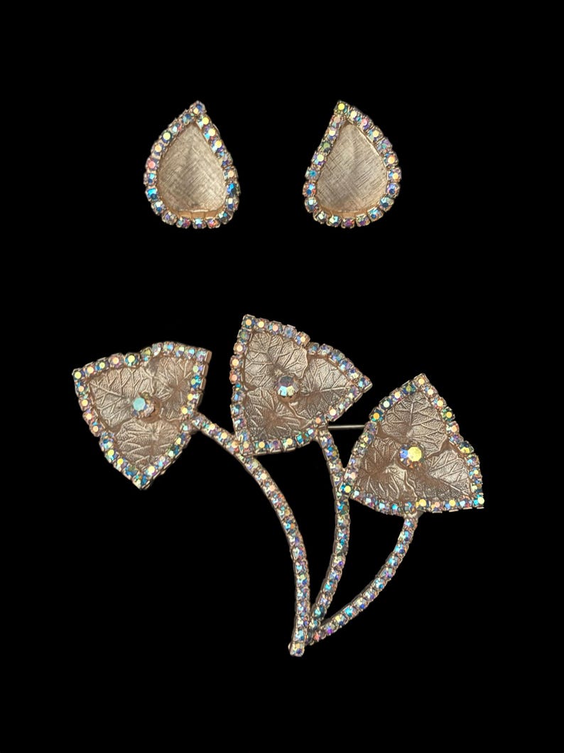Vertical front view of 1960s vintage iridescent rhinestone and gold tone floral brooch and clip on earring jewelry set.