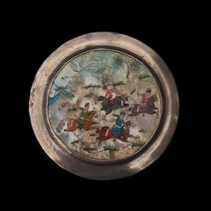 May include: A round, silver-toned plate with a detailed, colorful painting of figures on horseback in a landscape. The painting features riders in various outfits, set against a backdrop of trees and hills. The plate has a textured, aged appearance.