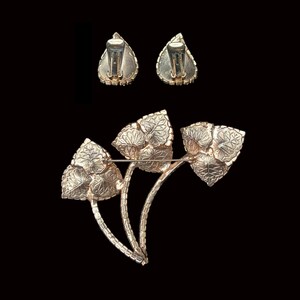 Horizontal back view of 1960s vintage iridescent rhinestone and gold tone floral brooch and clip on earring jewelry set.