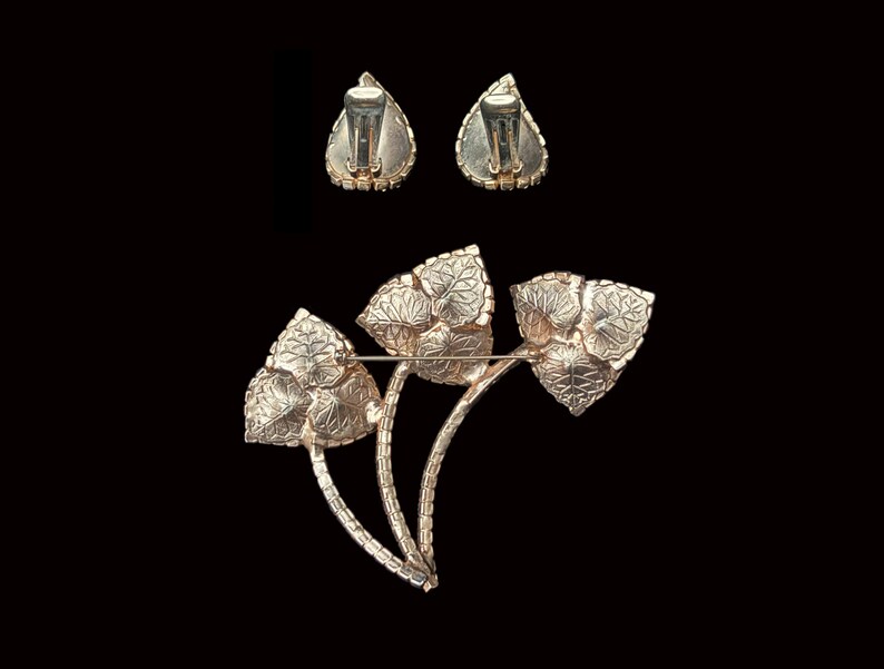 Horizontal back view of 1960s vintage iridescent rhinestone and gold tone floral brooch and clip on earring jewelry set.