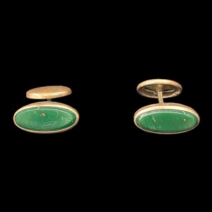 May include: A pair of oval-shaped cufflinks with a green stone inlay and gold metal accents.