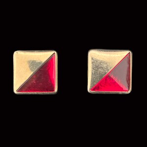 May include: A pair of gold and red square-shaped earrings. Each earring has a diagonal line dividing the square into two triangles, one gold and one red.