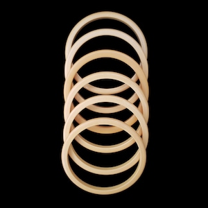 May include: A set of six wooden hoops, stacked in decreasing size, with a light brown color gradient. The hoops are arranged vertically, with the largest hoop at the top and the smallest hoop at the bottom.
