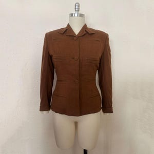 May include: A brown blazer with a tailored fit, displayed on a mannequin. The jacket features a notched collar, two front pockets, and button closures. The sleeves are long with buttoned cuffs. The blazer is a solid color.