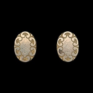 May include: A pair of silver oval-shaped cufflinks with a decorative swirl design.