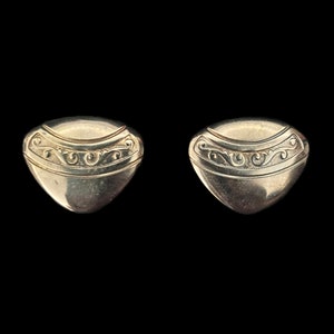May include: A pair of silver-toned earrings with a decorative design. The earrings are shaped like a teardrop with a curved top and a pointed bottom.