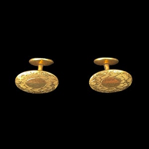 May include: A pair of gold cufflinks with a circular design. The cufflinks have a textured surface and a raised edge.